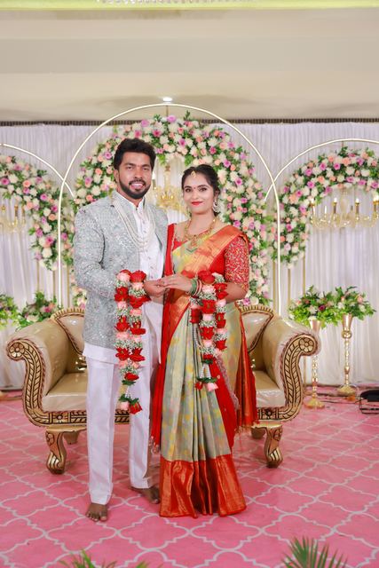 Akhil and Rachana on the engagement stage, garlanded, before a flower arch